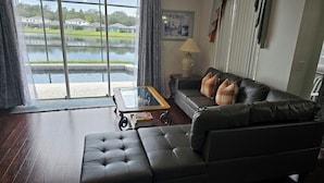 A living room with a leather sofa, a glass coffee table, and a view of a lake through large windows.
