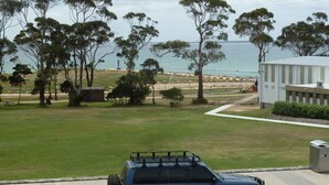 A view of a grassy area with trees, a beach, and a building with a white exterior.