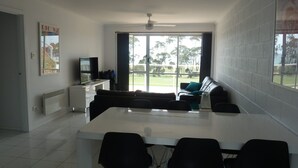 A modern living room with a large window, a white sofa, a TV, and a dining area with chairs.