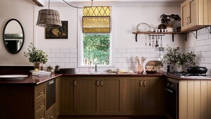 A kitchen with wooden cabinets, a window with a view of greenery, a hanging light fixture, and a shelf with dishes and utensils. - The Church at Lyonville ~ Daylesford Region (Lyonville)