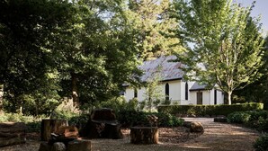 A rustic building with a white exterior and a rusted roof, surrounded by dense greenery and trees. - The Church at Lyonville ~ Daylesford Region (Lyonville)