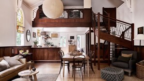 A spacious loft with a dining area, kitchen, and a wooden staircase. - The Church at Lyonville ~ Daylesford Region (Lyonville)