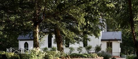 Een wit gebouw met een klein bijgebouw, omringd door bomen en een grindpad.