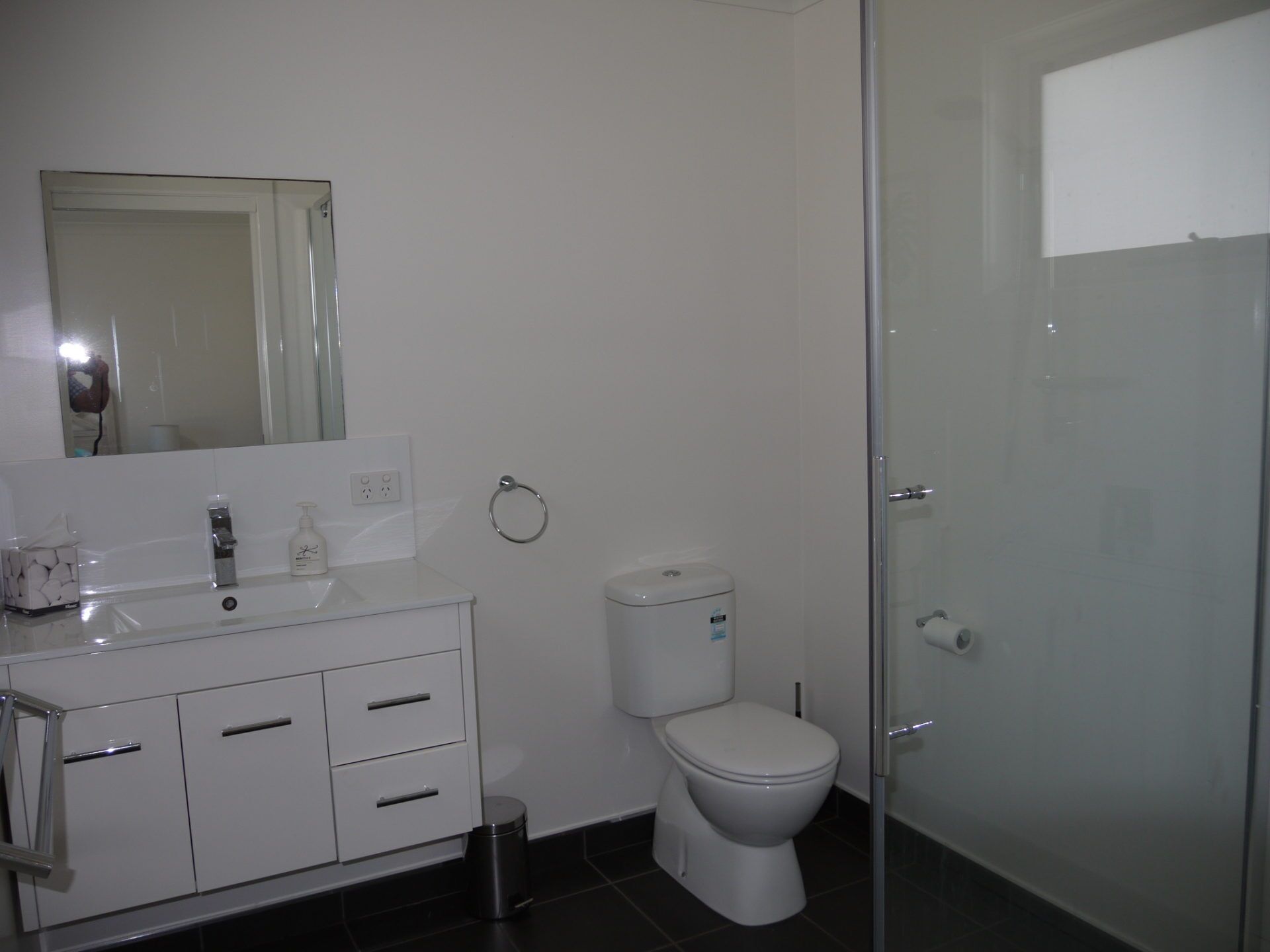 A modern bathroom with a white vanity, a toilet, and a glass shower enclosure.