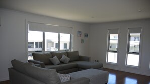 Un salon moderne avec un canapé d’angle gris, de grandes fenêtres et un plancher en bois franc.