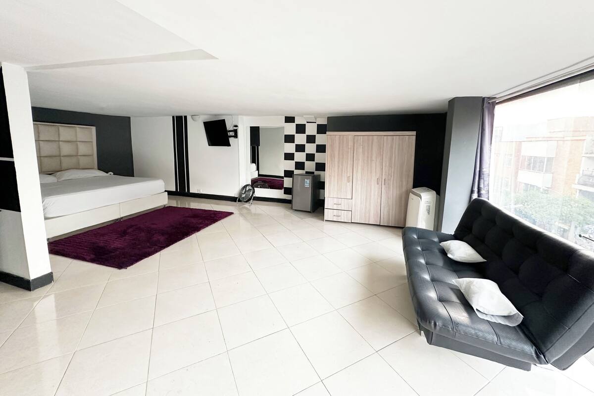 A modern, well-lit living room with a sofa, a bed, a large mirror, and a wardrobe.