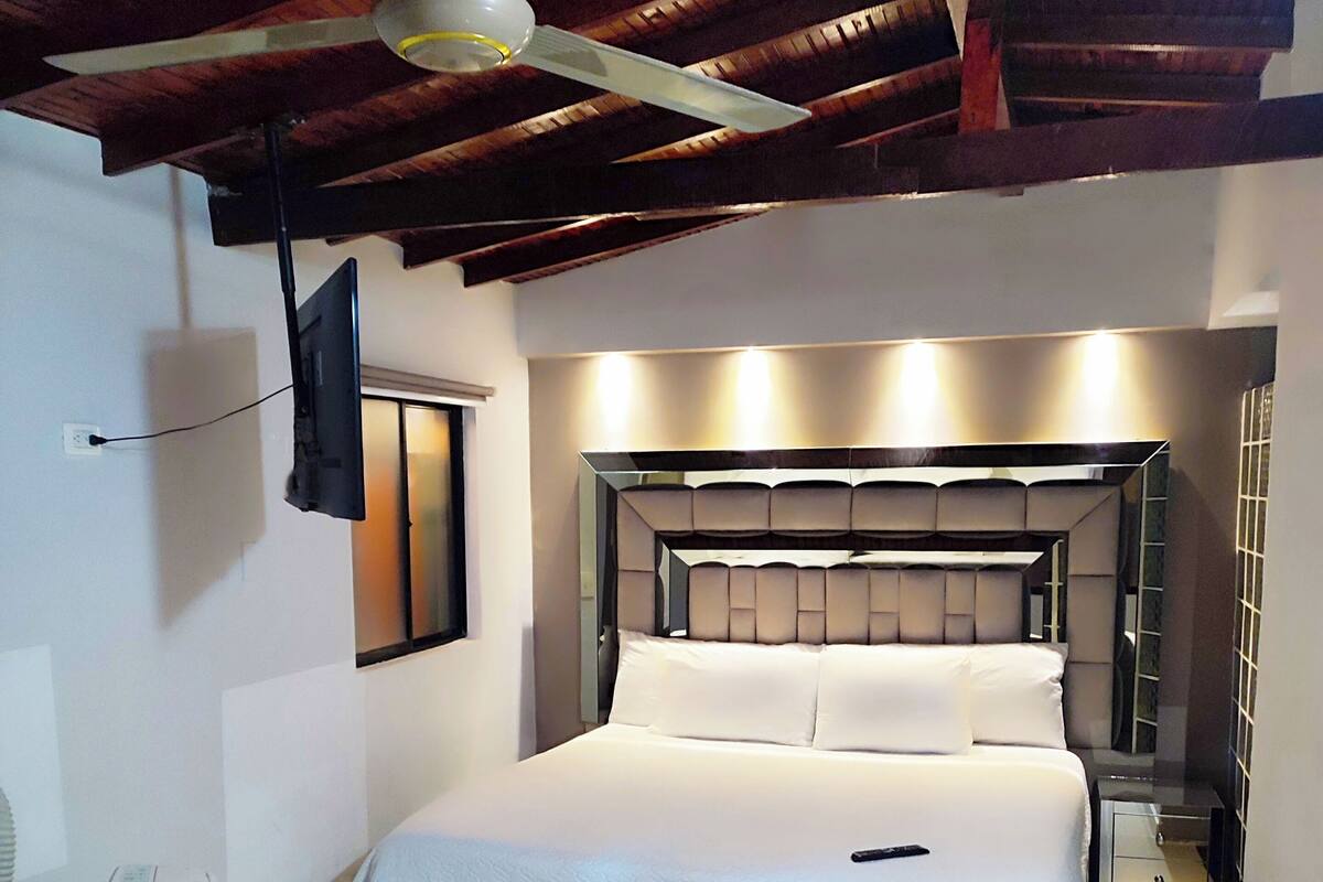 A bedroom with a bed, a ceiling fan, a TV mounted on the wall, and a bedside table.
