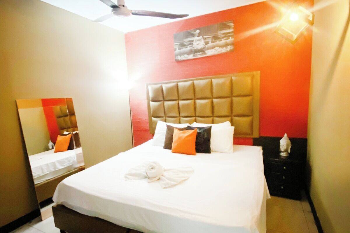 A hotel room with a bed, a ceiling fan, a nightstand, and a wall-mounted light fixture.