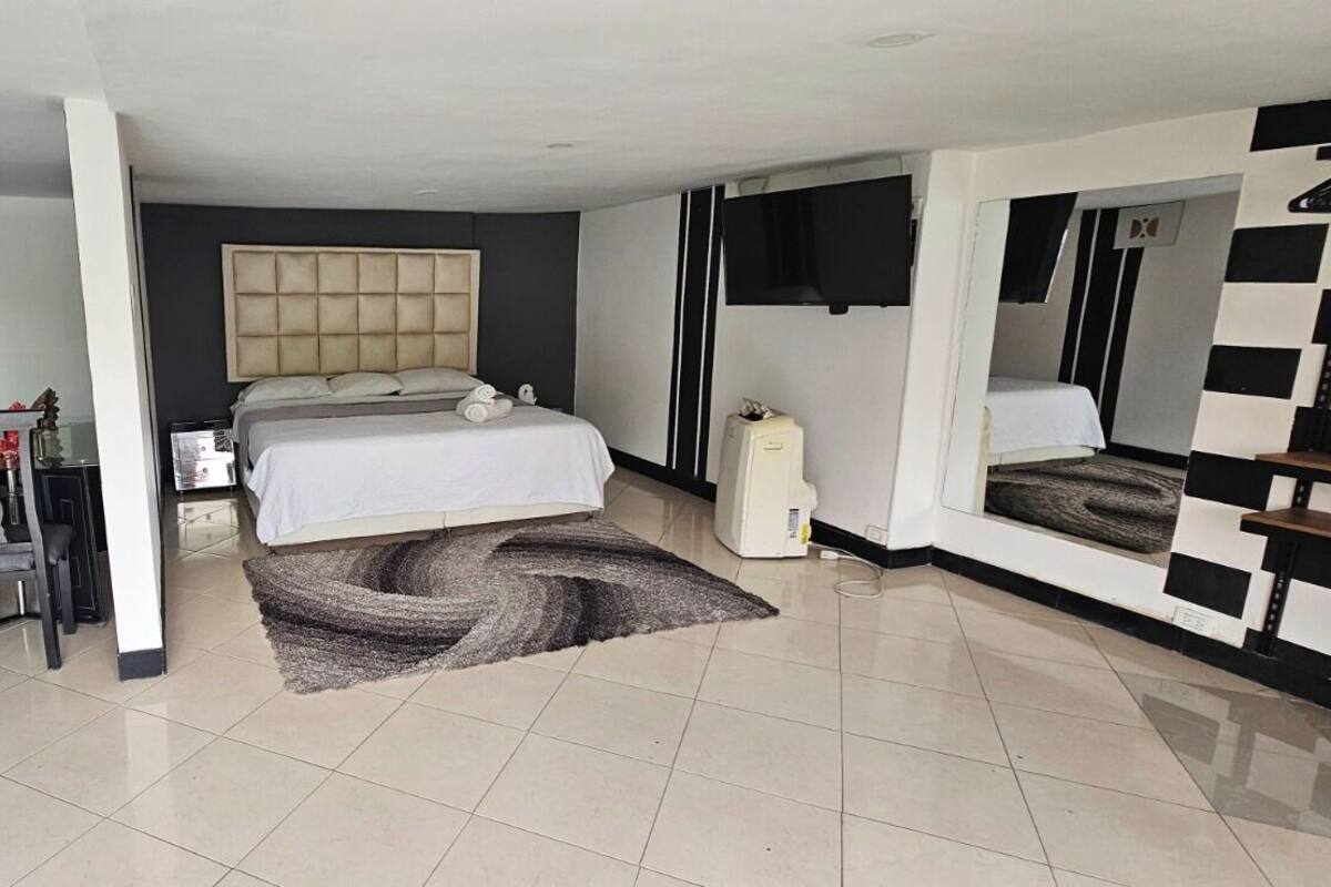 A bedroom with a bed, bedside tables, a desk, a chair, a TV, and a large mirror.