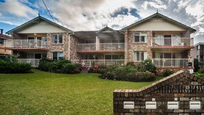 A three-story residential building with a brick facade, multiple balconies, and a well-maintained lawn. - Fully furnished 2 bedroom apartment (Mollymook)