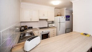 A small kitchenette with white cabinets, a microwave, a toaster, and a refrigerator. - Fully furnished 2 bedroom apartment (Mollymook)
