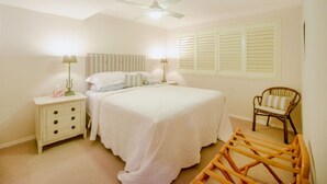 A bedroom with a bed, nightstands, a chair, a ceiling fan, and a window with shutters. - Fully furnished 2 bedroom apartment (Mollymook)