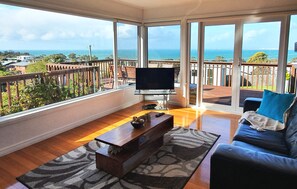 A living room with a large TV, wooden coffee table, and a sofa with a blue pillow. - Fabulous Ocean Views (Bridport)