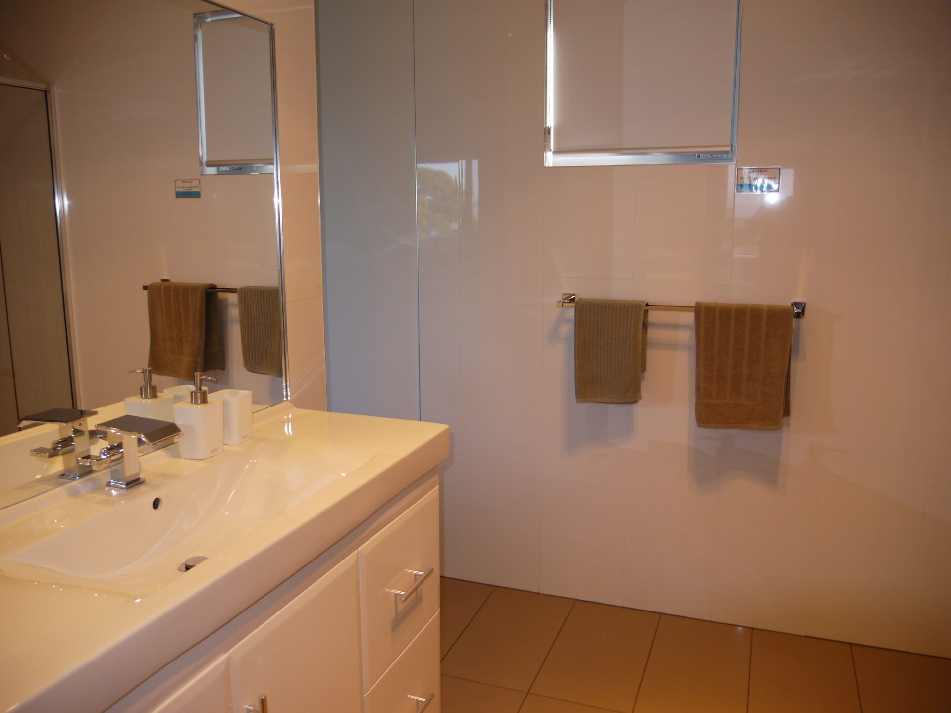 Une salle de bain moderne avec un grand miroir, un lavabo blanc et deux serviettes suspendues à des porte-serviettes.
