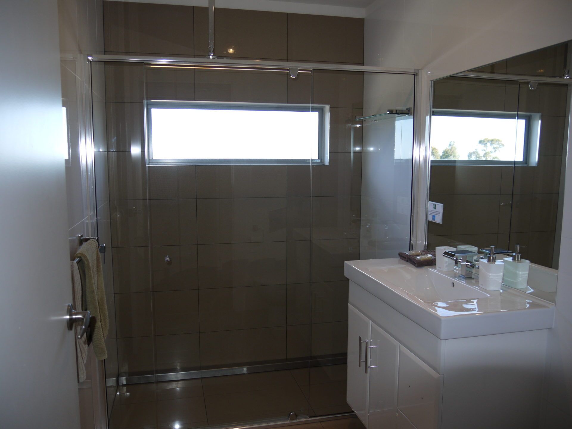 A modern bathroom with a glass shower enclosure, a large mirror, and a white vanity with toiletries.