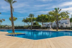 Una piscina con bordeado de baldosas, rodeada de palmeras y un edificio con balcones.
