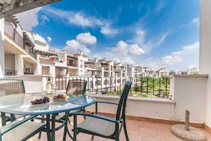 A terrace with a glass table and chairs, a bowl of fruit, and a bottle of wine.