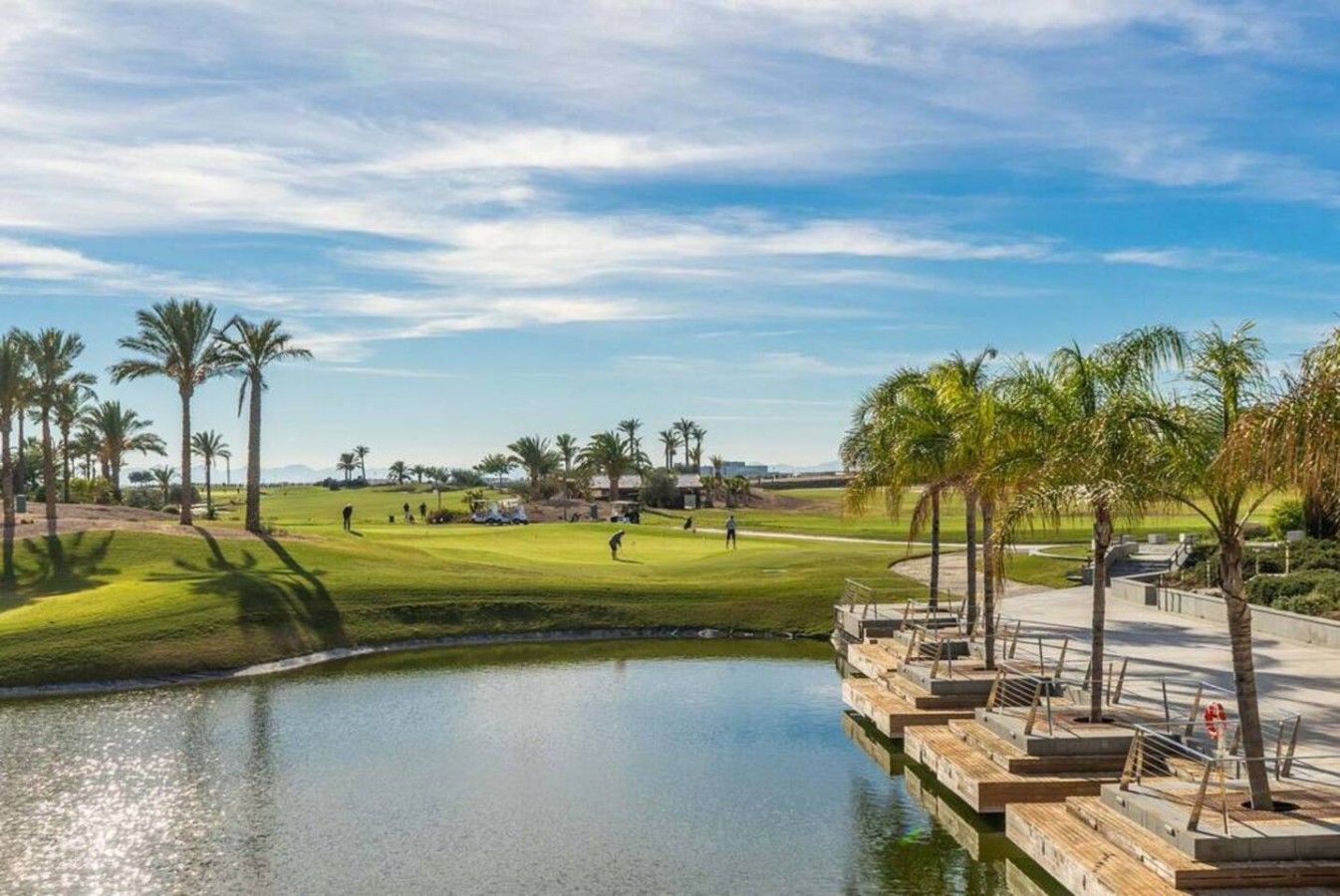 A golf course with a pond, palm trees, and a clear sky.