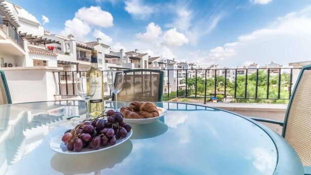 Ein Glastisch mit einer Schüssel Trauben und einem Teller Croissants auf einem Balkon mit Blick auf eine Wohngegend.