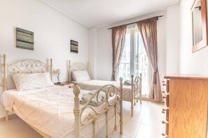 Une chambre avec deux lits, une commode en bois et une fenêtre avec des rideaux.