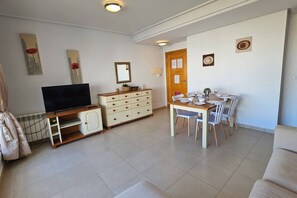 Una sala de estar con televisor, una mesa de comedor para dos personas, un sofá y un aparador.