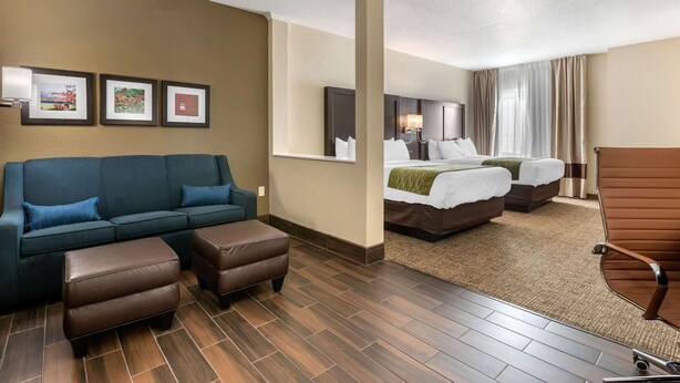 Una habitación de hotel con sofá, dos otomanas, una cama con manta verde y una silla.
