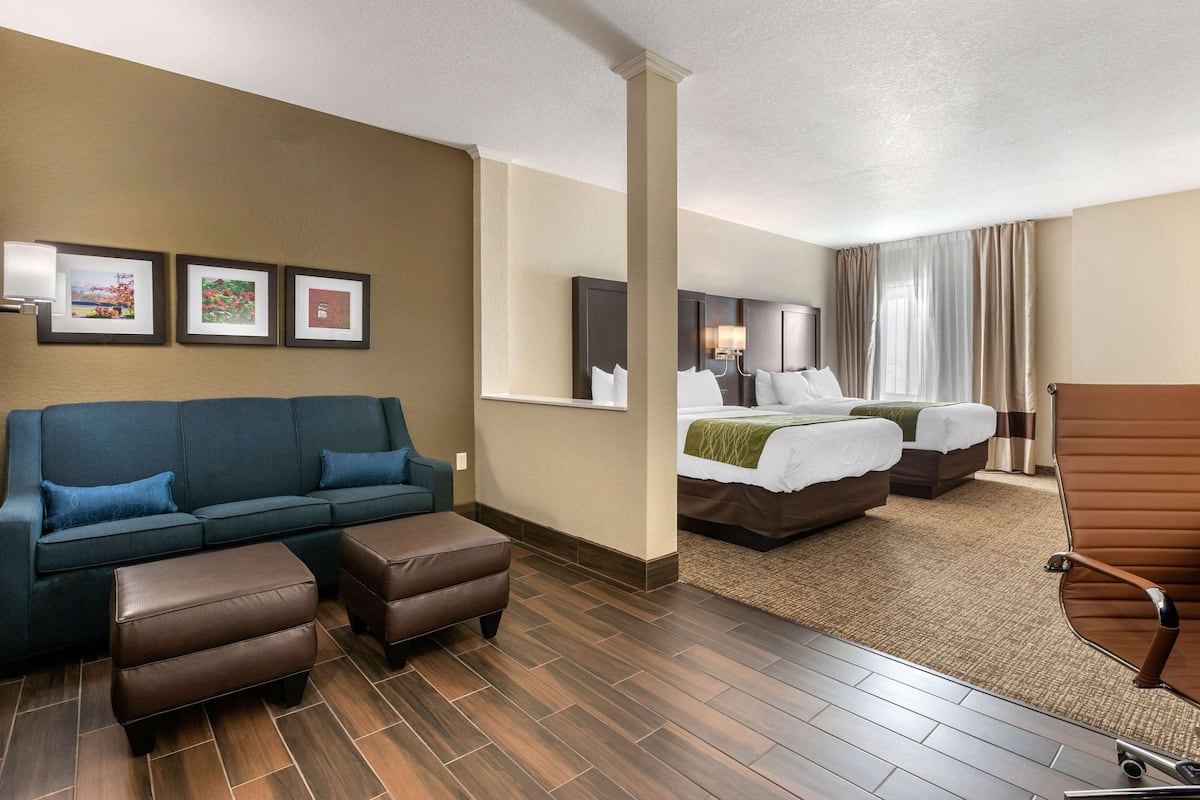 Una habitación de hotel con sofá, dos otomanas, una cama con manta verde y una silla.