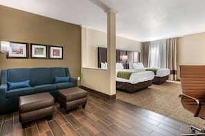 A hotel room with a sofa, two ottomans, a bed with a green blanket, and a chair. - Comfort Inn & Suites Cedar Rapids CID Eastern Iowa Airport (Cedar Rapids)