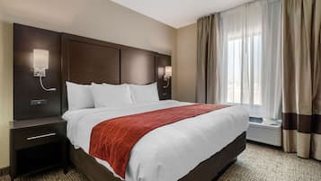 Habitación de hotel con una cama grande, una mesita de noche, una lámpara de pared y una ventana con cortinas.