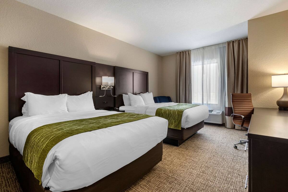 Habitación de hotel con dos camas, un escritorio, una silla y un amplio ventanal con cortinas.
