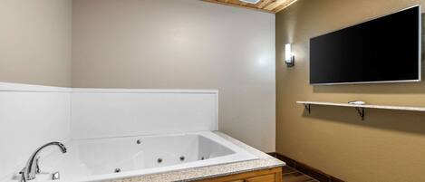 Un baño moderno con una bañera independiente, muebles de madera, un televisor montado en la pared y piso de baldosas.