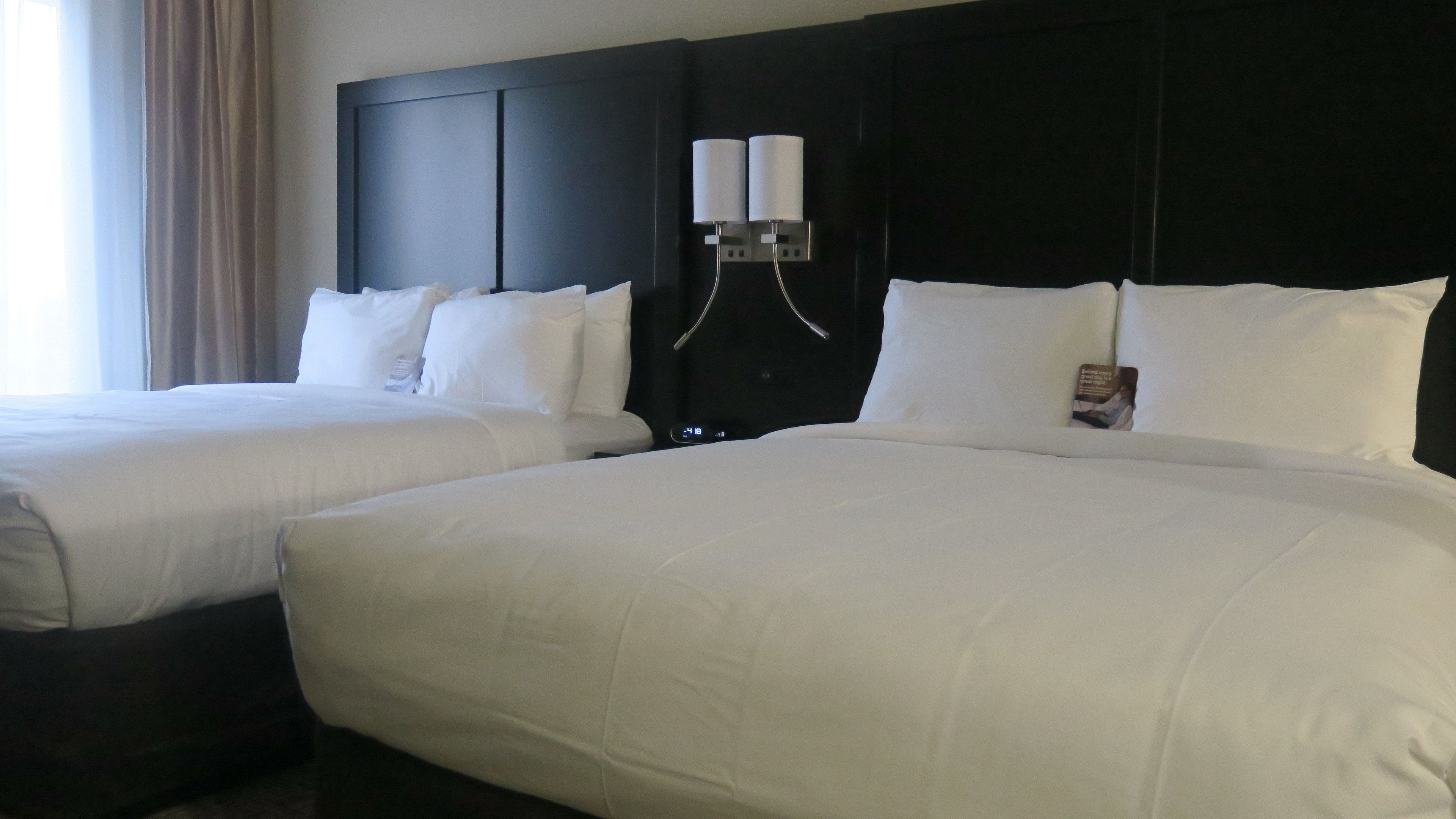 Habitación de hotel con dos camas grandes, un cabecero oscuro y una mesita de noche con dos lámparas.