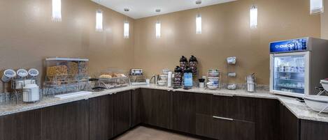 Un'area colazione in hotel con angolo self-service, un frigorifero e una macchina per il caffè.