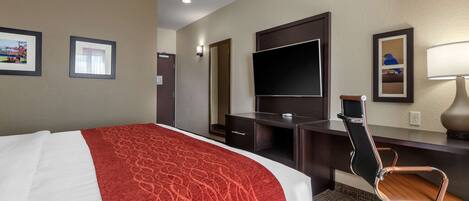 A hotel room with a bed, a desk, a chair, a TV, and framed pictures on the wall.