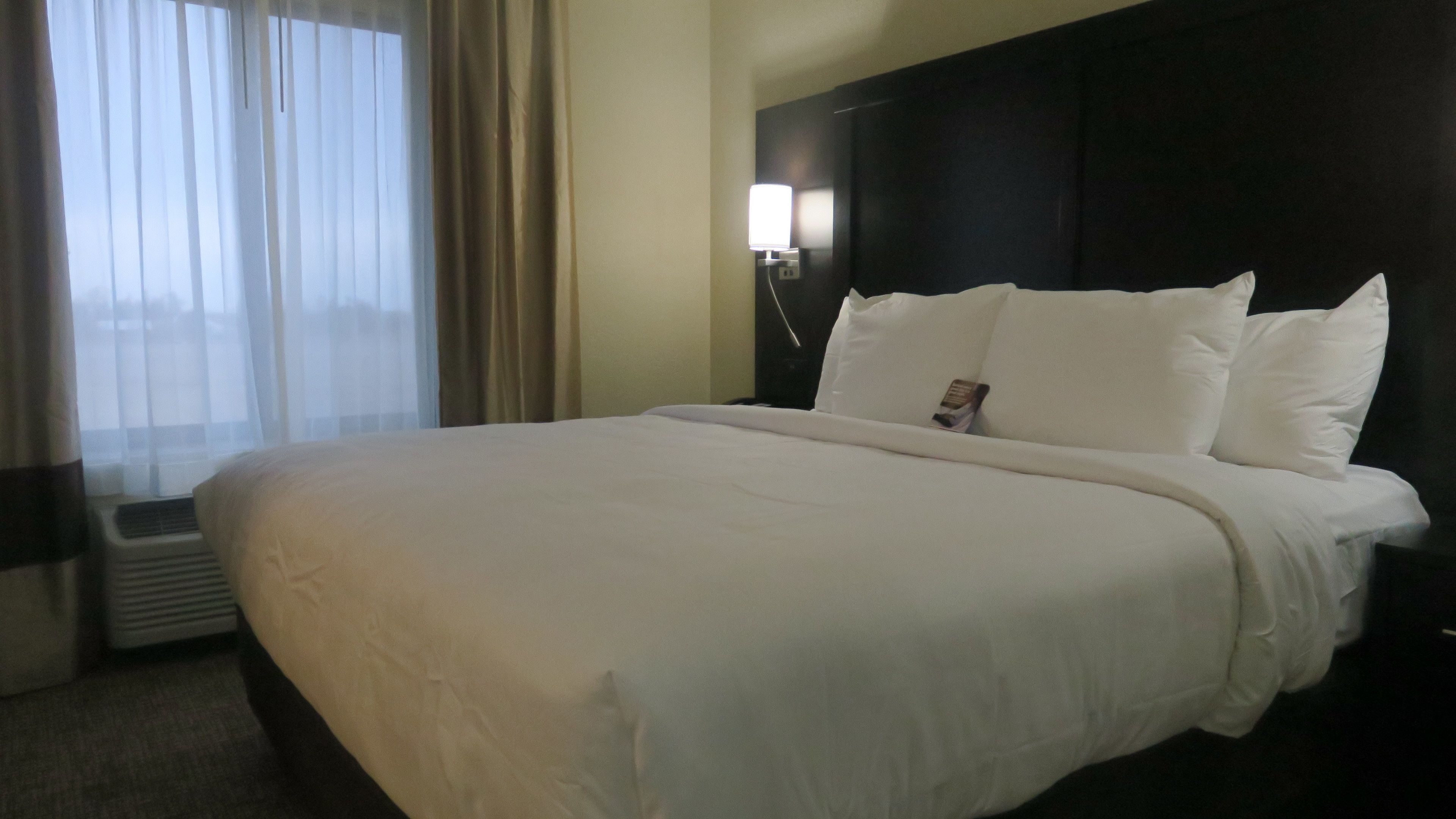 A hotel room with a large bed, a bedside lamp, and a window with curtains.
