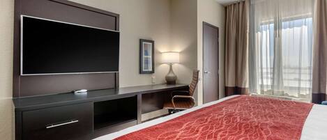 Una habitación de hotel con una cama grande, un televisor de pantalla plana montado en la pared, un escritorio con lámpara y una ventana con cortinas.