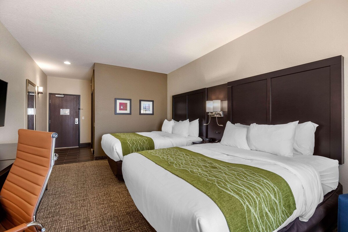 A hotel room with two beds, a sitting area with a chair, a desk, and a lamp.