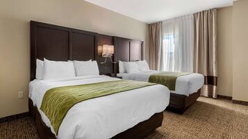 A hotel room with two beds, a headboard with a light fixture, and a large window with curtains.