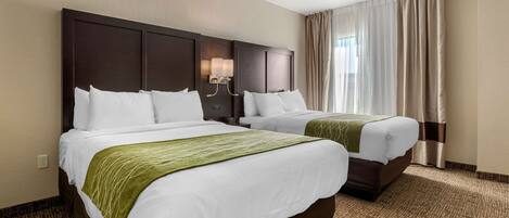 Habitación de hotel con dos camas, cabecera con lámpara y una ventana grande con cortinas.