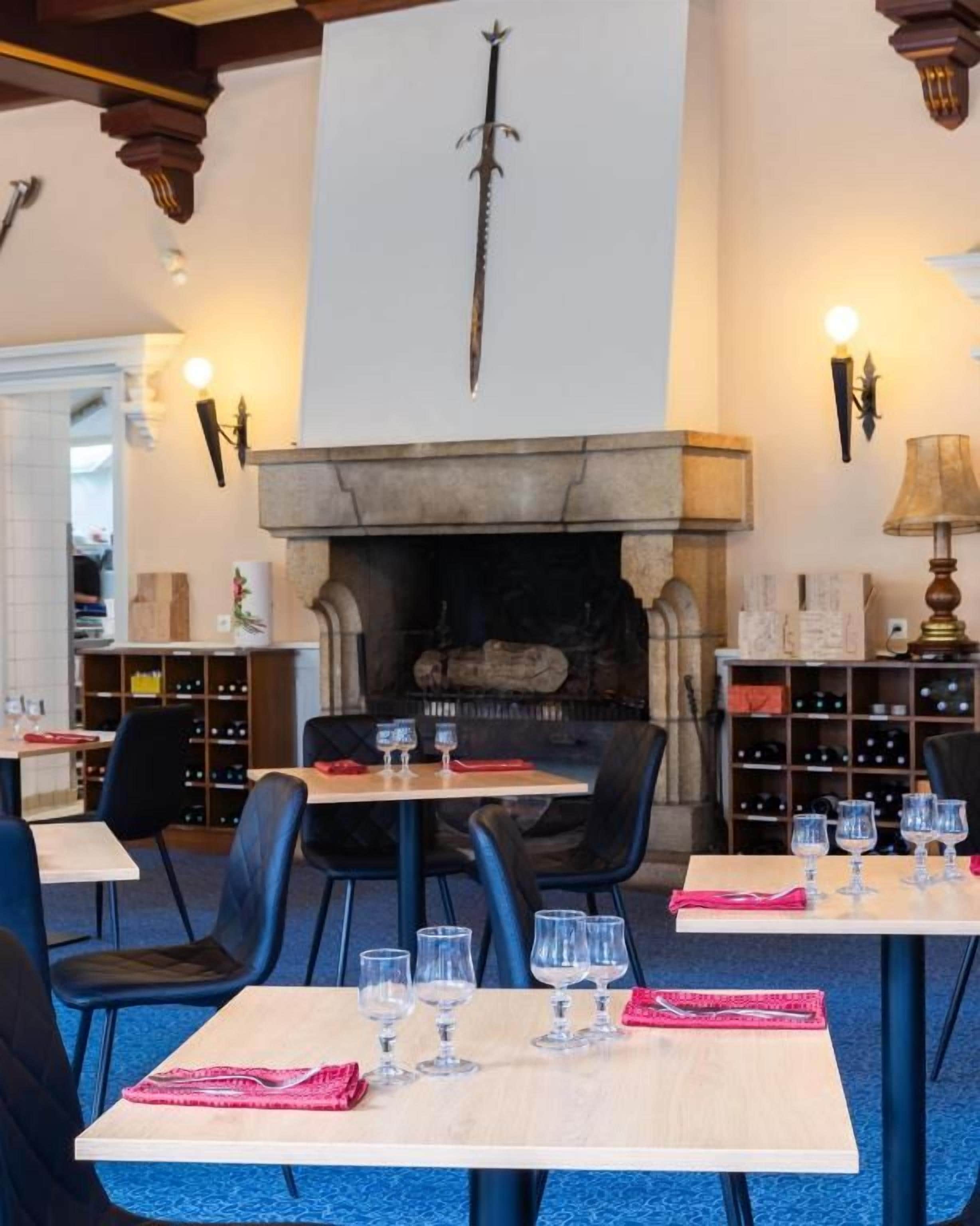 Interior de restaurante com mesas montadas para refeições, lareira e estantes de vinho ao fundo.