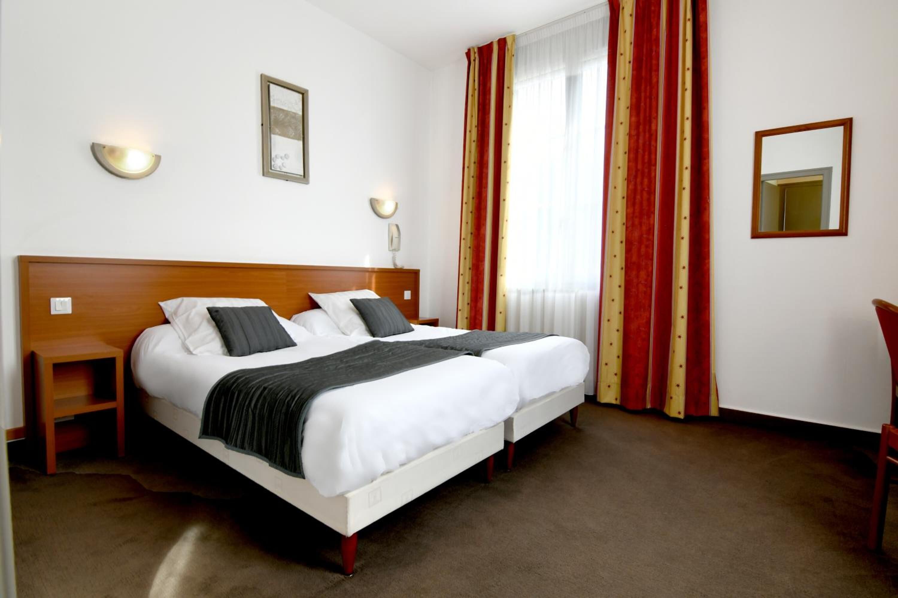 Un lit double avec deux oreillers, une table de chevet, une commode, un miroir et une fenêtre avec des rideaux rouges.