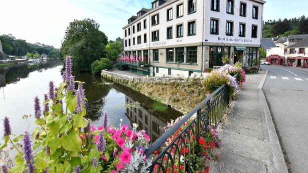 A hotel with a river view, a covered outdoor seating area, and a garden with flowers. - Logis Hotel du Chateau (Josselin)