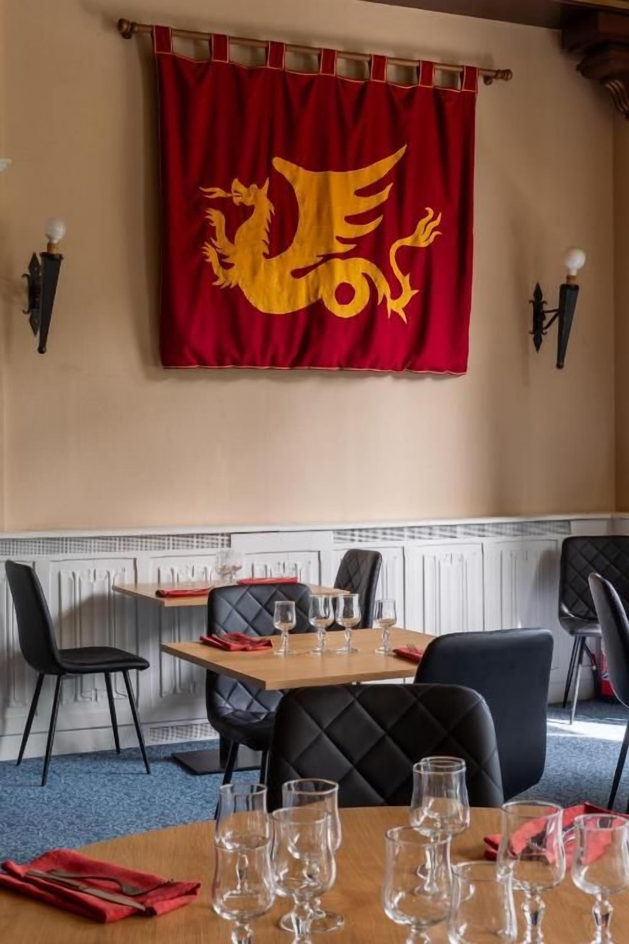 A dining area with a table set for four, chairs, and a red flag with a golden dragon design on the wall.