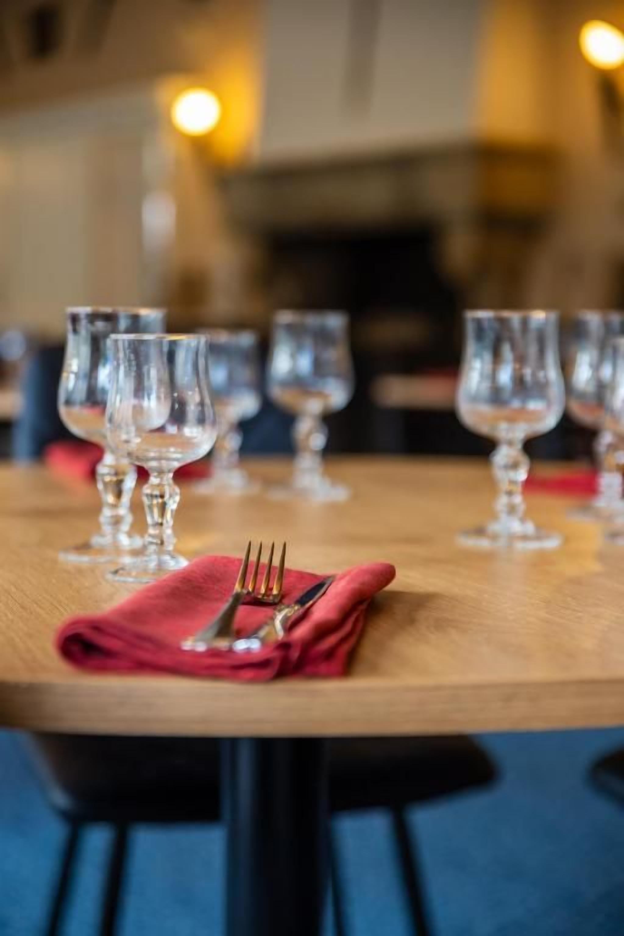 A dining table with multiple wine glasses and a folded red napkin with cutlery.