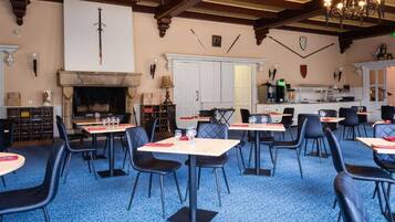 A dining area with tables and chairs, a fireplace, and a kitchen in the background.