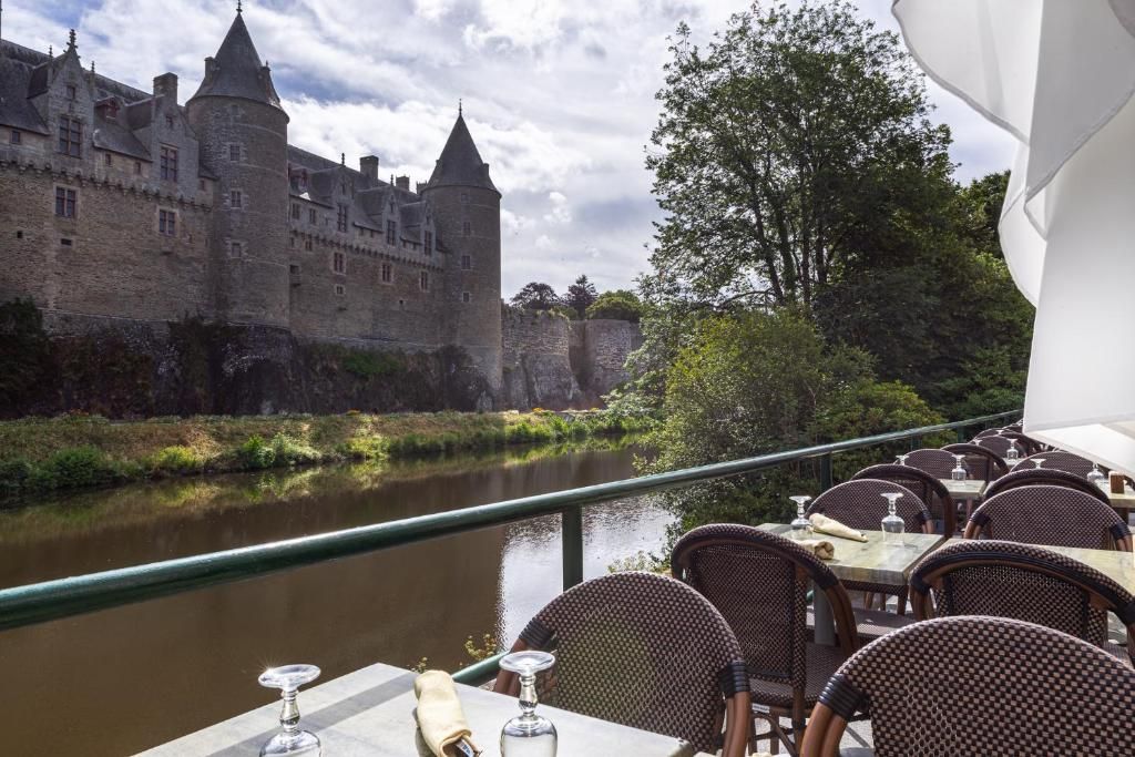 Een eetgedeelte aan de waterkant met tafels en stoelen, met uitzicht op een historisch kasteel.