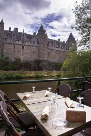 An outdoor dining table with chairs, a menu, and a view of a castle. - Logis Hotel du Chateau (Josselin)