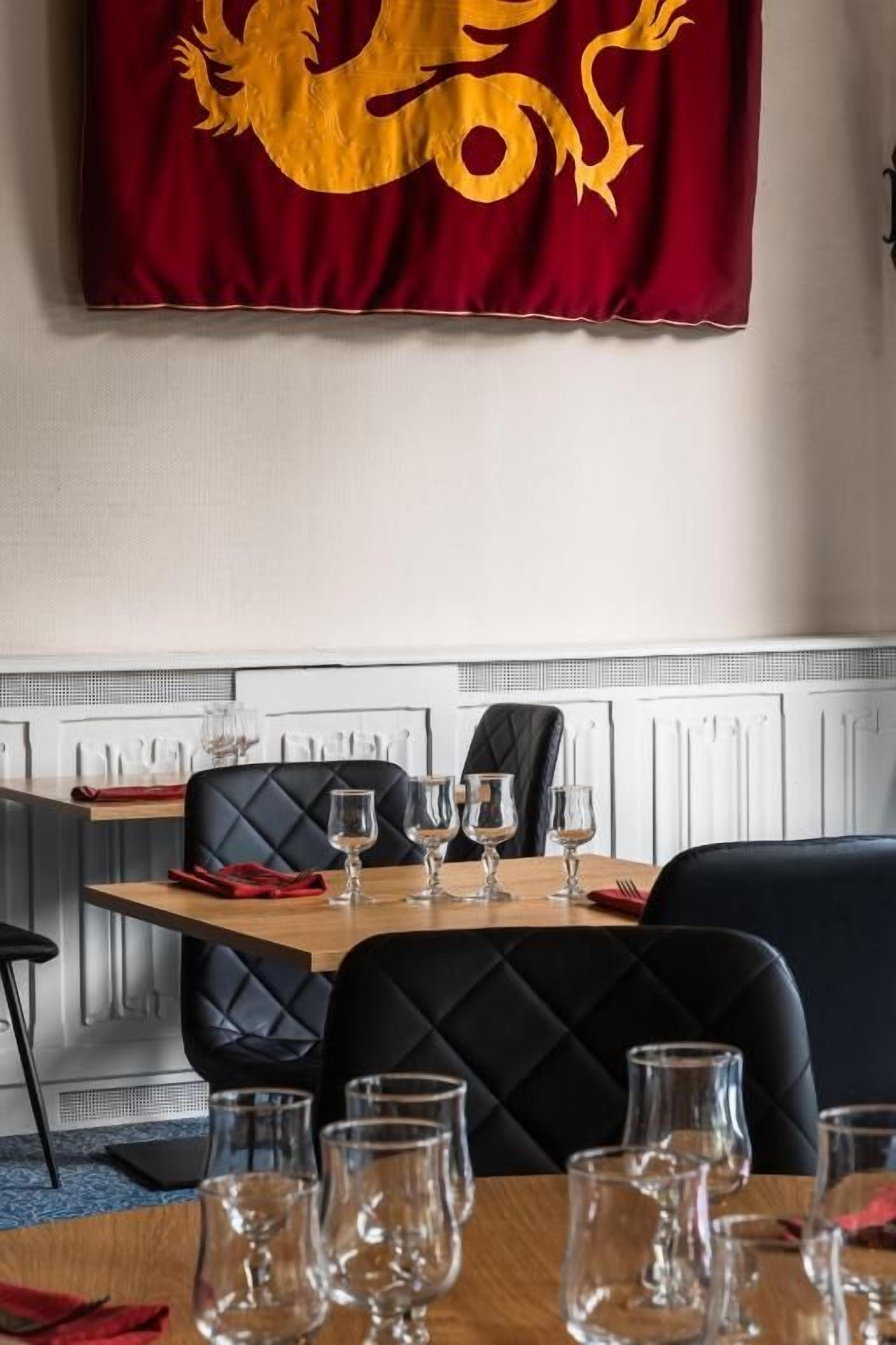 A dining area with a table set for four, a red flag with a golden dragon, and black upholstered chairs.