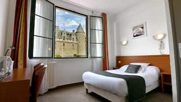 A hotel room with a large window offering a view of a castle, a bed with white linens, a bedside table, and a chair.