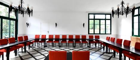 Un salón de conferencias con mesas largas y sillas rojas, ventanas amplias y candelabros negros.